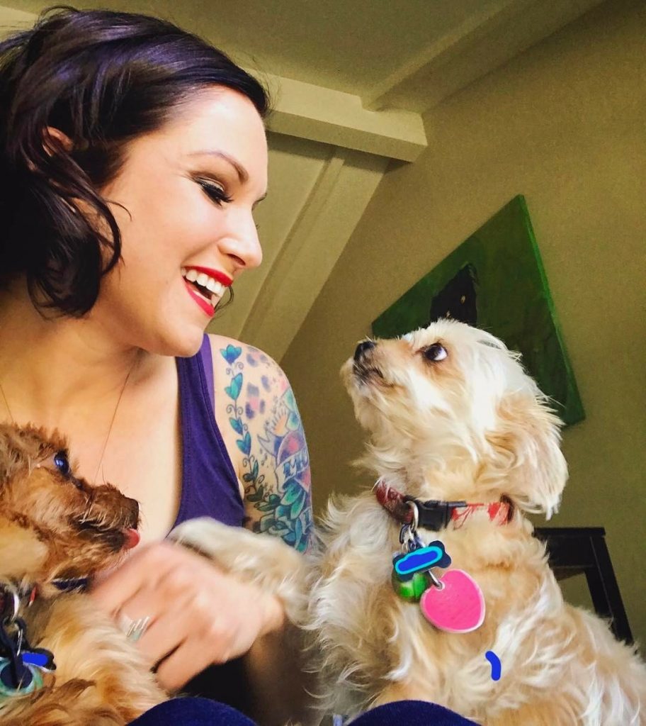 Dog Trainer Cora Wittekind smiles at happy white dog while holding another small dog